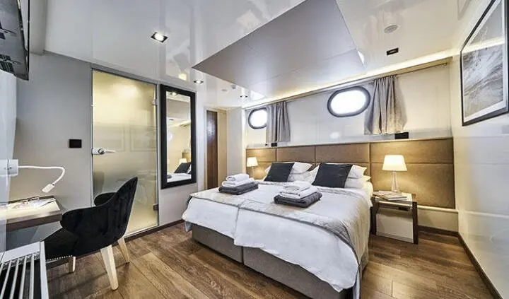 Rara Avis yacht cabin with double bed, ensuite, wood floors, portholes, and seating