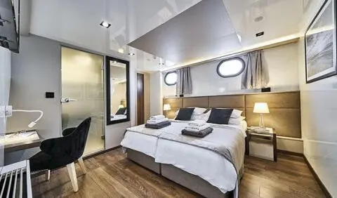 Rara Avis yacht cabin with double bed, ensuite, wood floors, portholes, and seating