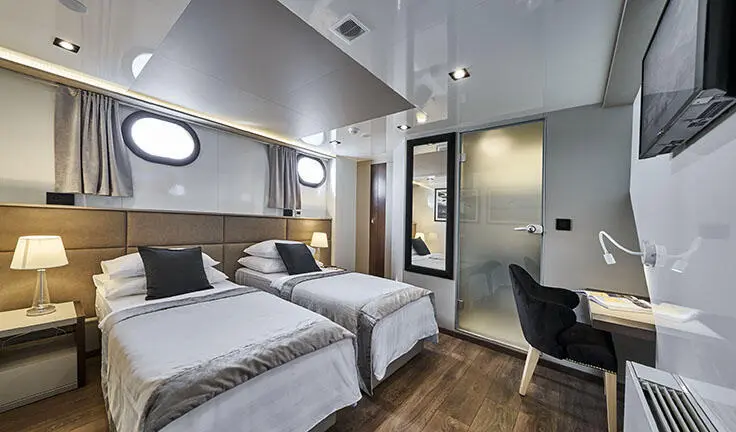 Twin cabin with two single beds, ensuite bathroom, wooden floor, grey bedding