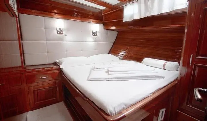 Malena yacht cabin with double bed, white linens, wooden walls and built-in storage