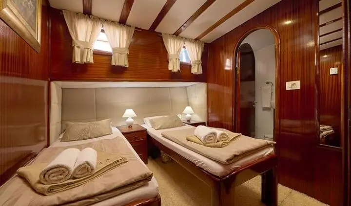 Twin-cabin interior with wooden paneling, bed, seating area, and ensuite door