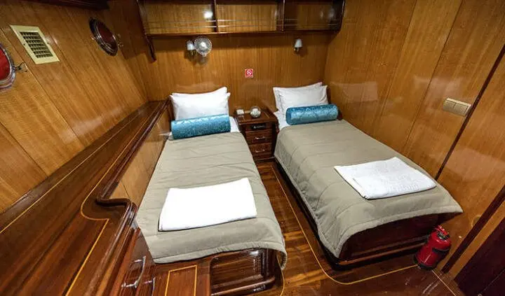 Two single beds in a wood-paneled cabin with blue pillows and white linens