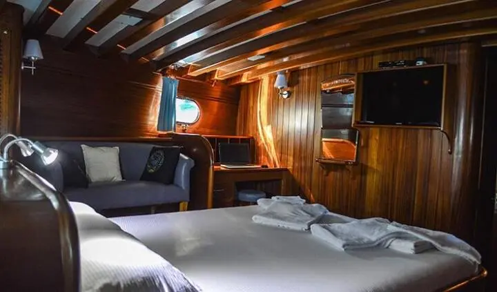 Cozy king bed in wood-paneled yacht cabin with seating area and ensuite doorway