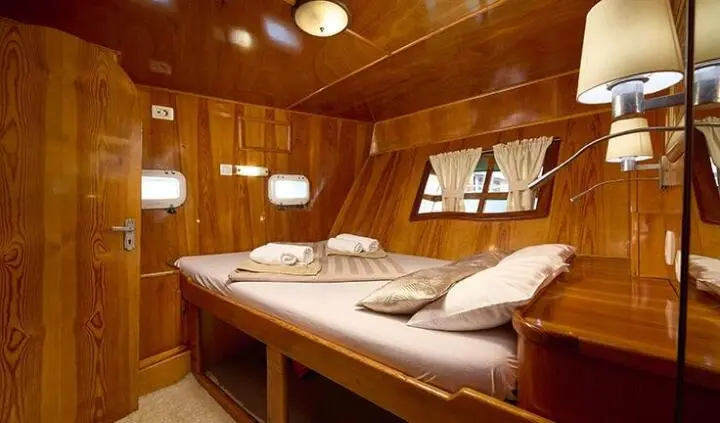 Interior of a wood-toned yacht cabin with two single beds and cushions