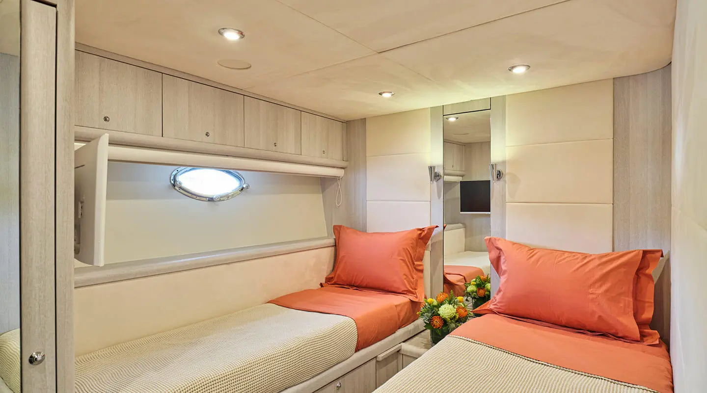 Interior of M Five yacht: cream walls, beige seating, orange cushions, round porthole, small table with flowers