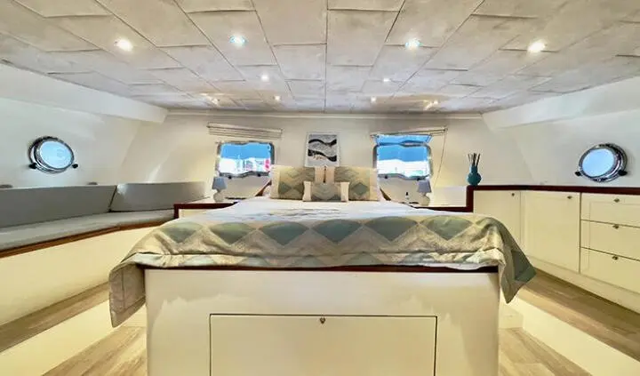 Master cabin with large bed, beige upholstery, and overhead cabinets on the yacht