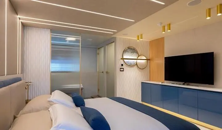 Master cabin with king bed, white bedding, blue accent pillows, ensuite door