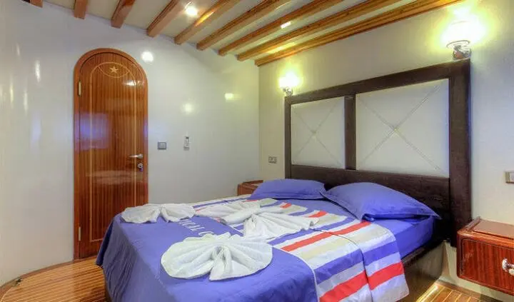 Master cabin with king bed, two navy blue bedspreads and wooden ceiling beams
