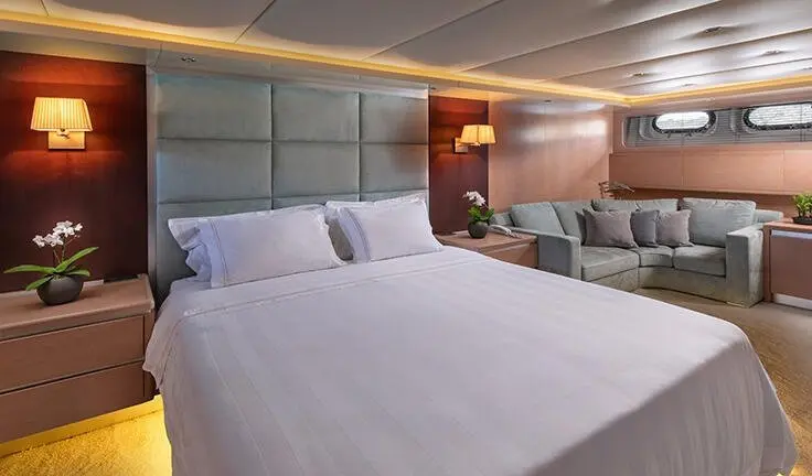 Master cabin with large bed, white linens, padded headboard, and seating area