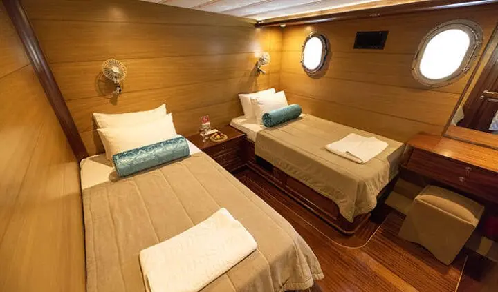 Twin cabin with two single beds, wood paneling, towels folded at foot