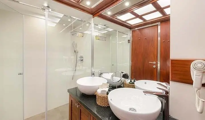 Yacht Lady Gita cabin bathroom with glass shower, dual sinks, wood cabinetry