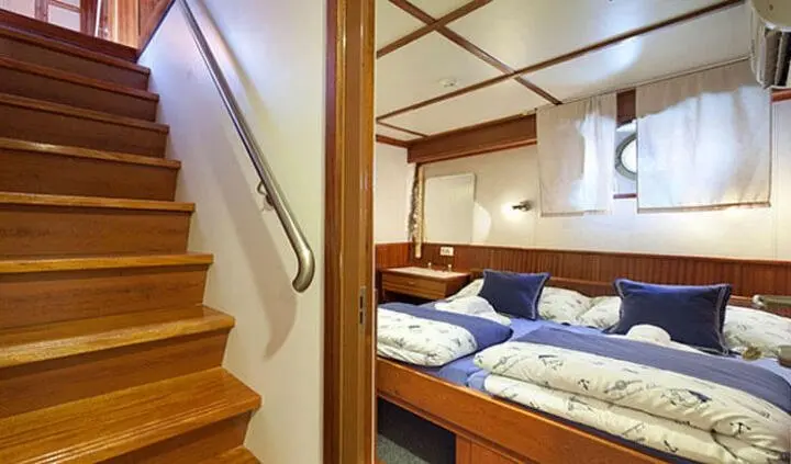 View of a wooden boat cabin with blue and white bed linens and stairs