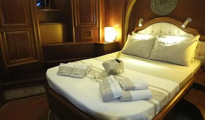 Master cabin with king bed, wooden panels, bedside lamps, towels on bed