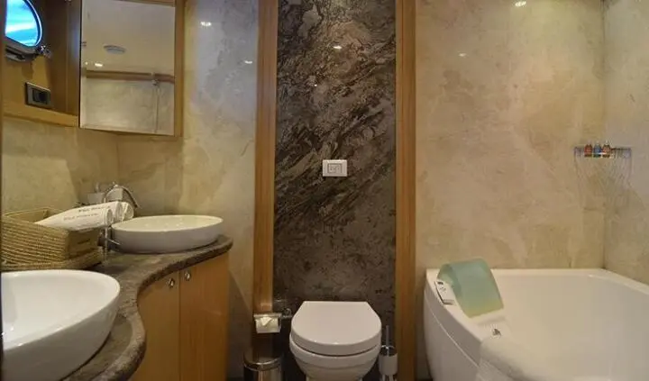 Compact yacht cabin with toilet, sink, and shower area between dual beds