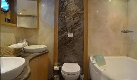 Compact yacht cabin with toilet, sink, and shower area between dual beds