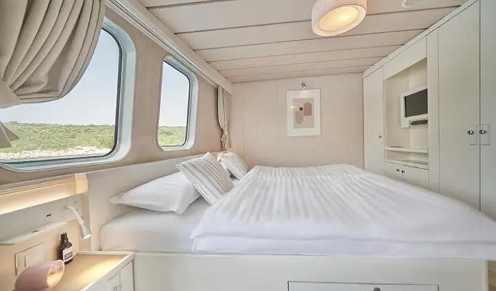 Bright yacht cabin with a large bed, white linens, and windows
