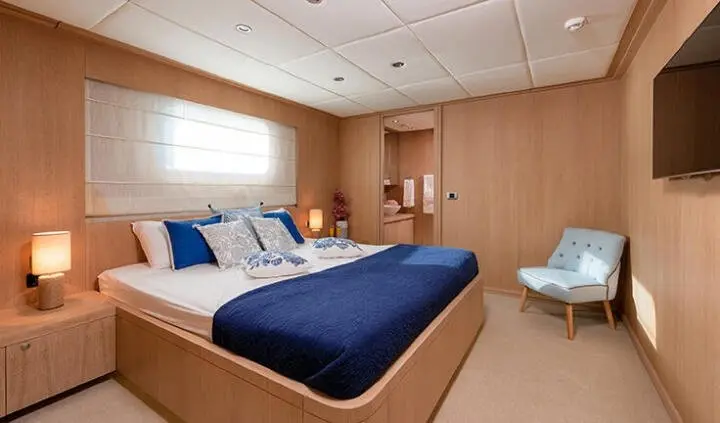 Grace yacht cabin with queen bed, navy bedding, wood walls, window light