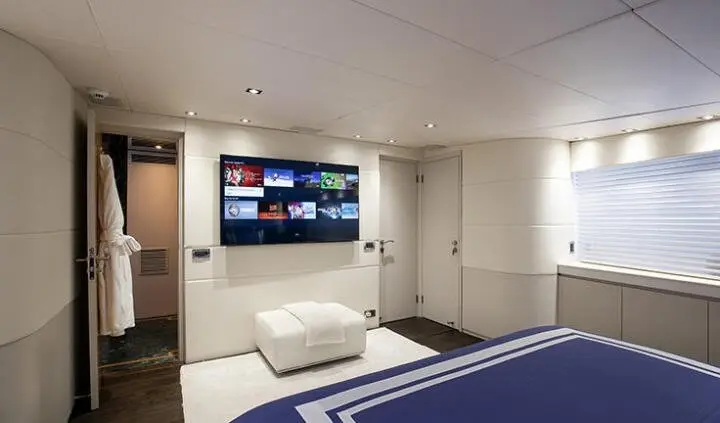 Master cabin with king bed, white cushions, and a wall-mounted TV screen