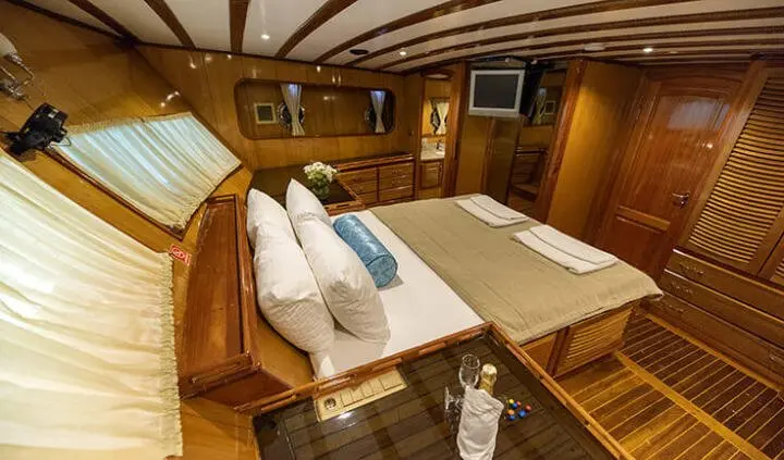 Master cabin with king bed and two nightstands, wooden panels and ensuite doorway