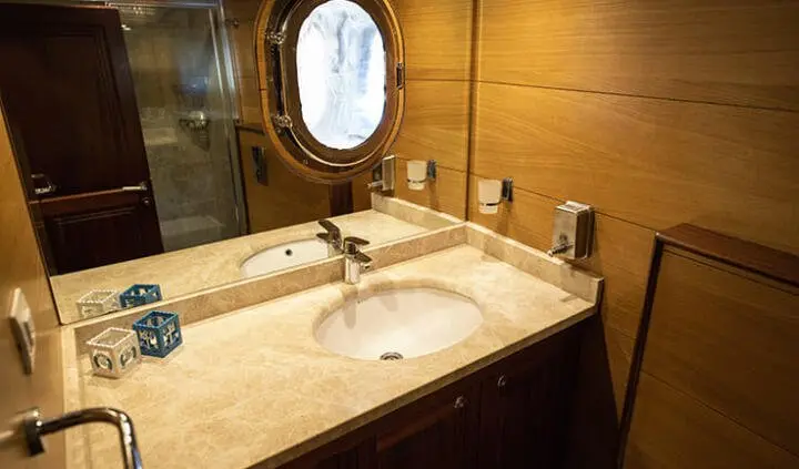 Cabin vanity area on Kayhan 4 yacht; sink, mirror, and brown wood paneling