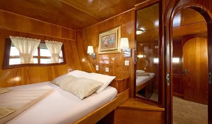 Interior of Linda yacht cabin with double bed, wooden panels, and warm lighting
