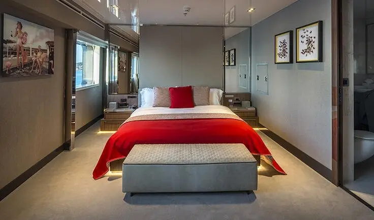 Master cabin with a king-size bed, red bed runners, and a cushioned bench