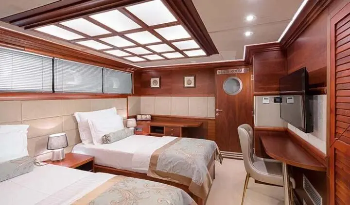 Twin cabin on Lady Gita yacht with two single beds, wood paneling, and porthole windows