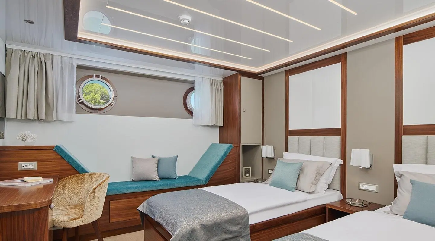 Luxurious yacht Corsario interior with two sunbeds, teal cushions, wooden panels, and large window views