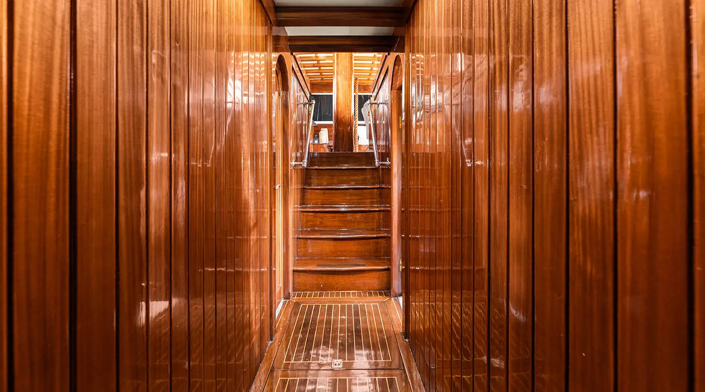 Wooden interior corridor of a classic yacht with polished teak walls and a stairway ahead