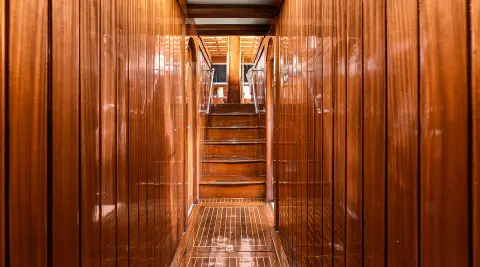 Wooden interior corridor of a classic yacht with polished teak walls and a stairway ahead