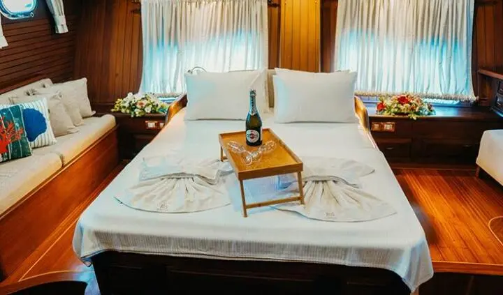 Twin white cabins with bed setup and pillow, wooden table on deck