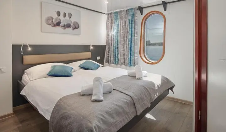 Master cabin with king bed, gray bedding, round mirror, and porthole window