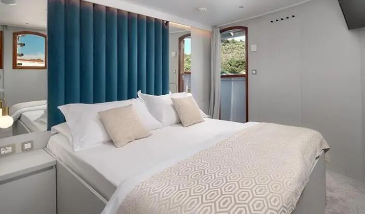 Master cabin with king bed, white bedding, beige pillows, blue curtains, natural light