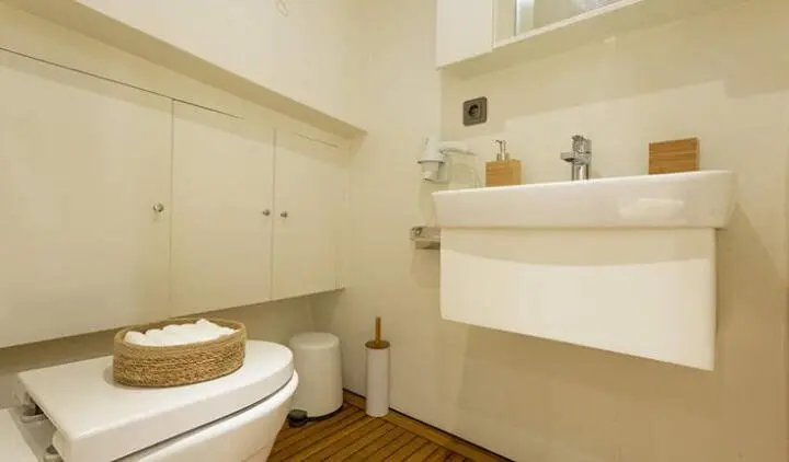 Compact yacht cabin with bed, ensuite bathroom, sink, and storage shelves