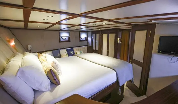 Gazella yacht cabin with two twin beds, wood paneling, porthole windows, and ceiling beams