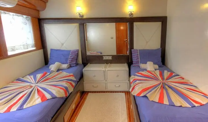 Twin cabin with two single beds, vibrant striped duvets and a central dresser