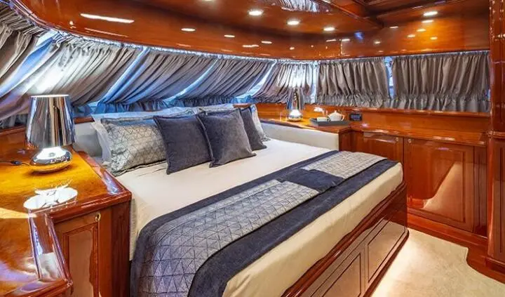 A spacious yacht master cabin with a large bed, blue-gray linens, and wooden cabinetry.