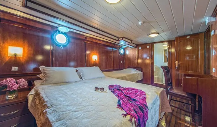 Master cabin on Luna yacht with large bed, purple throw, wood paneling