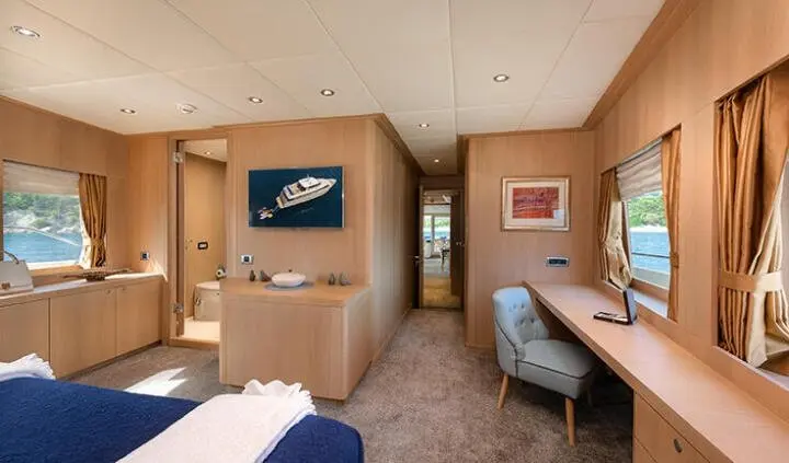 Grace yacht cabin with blue bed, wooden cabinets, desk, and small window view