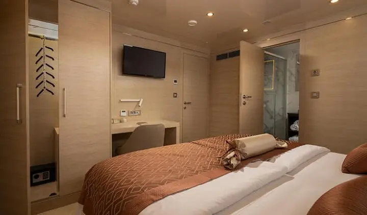 Two beds in a cabin with beige walls, brown duvets, and a wall-mounted TV