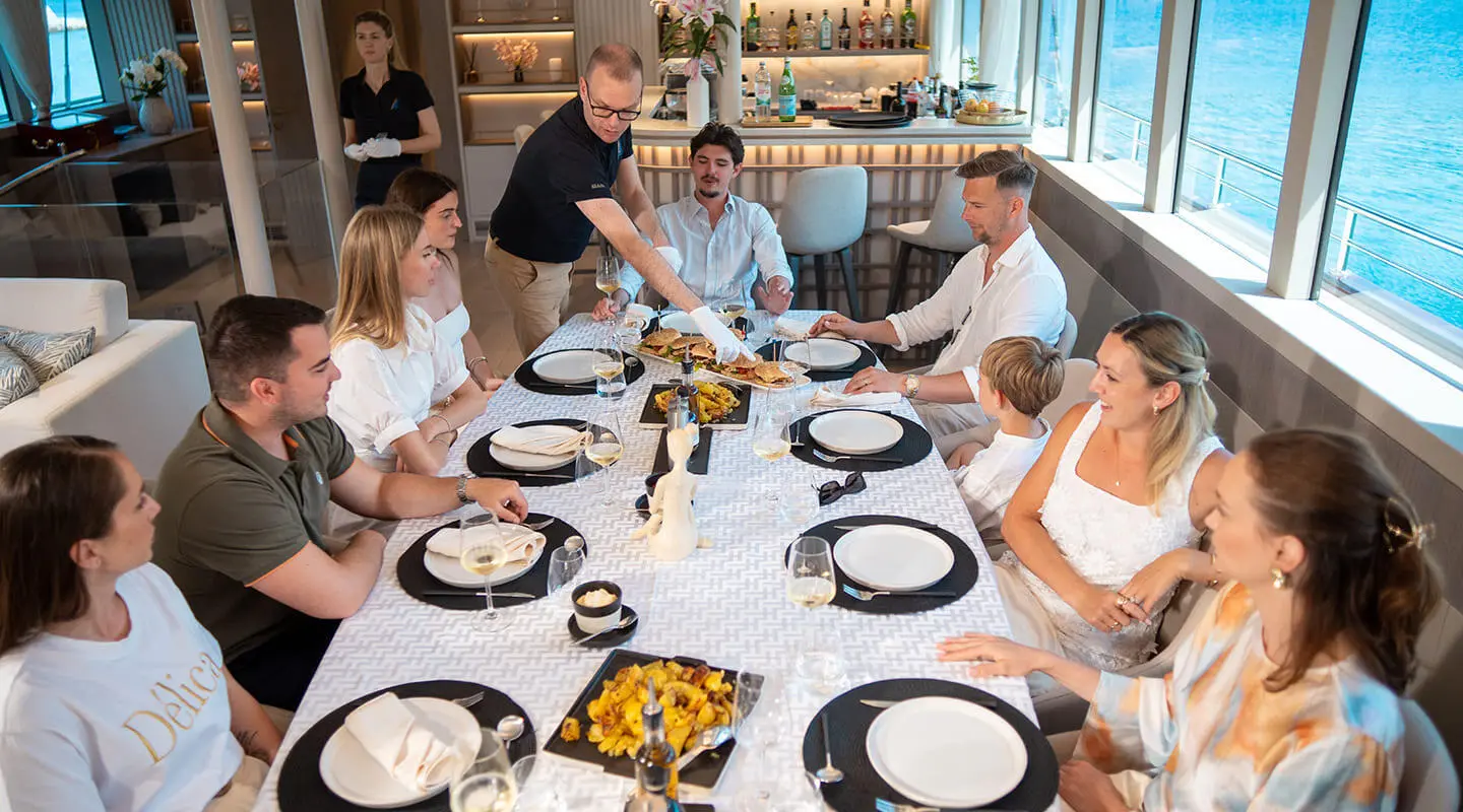 Nocturno yacht dining scene at sunset with guests around a long table