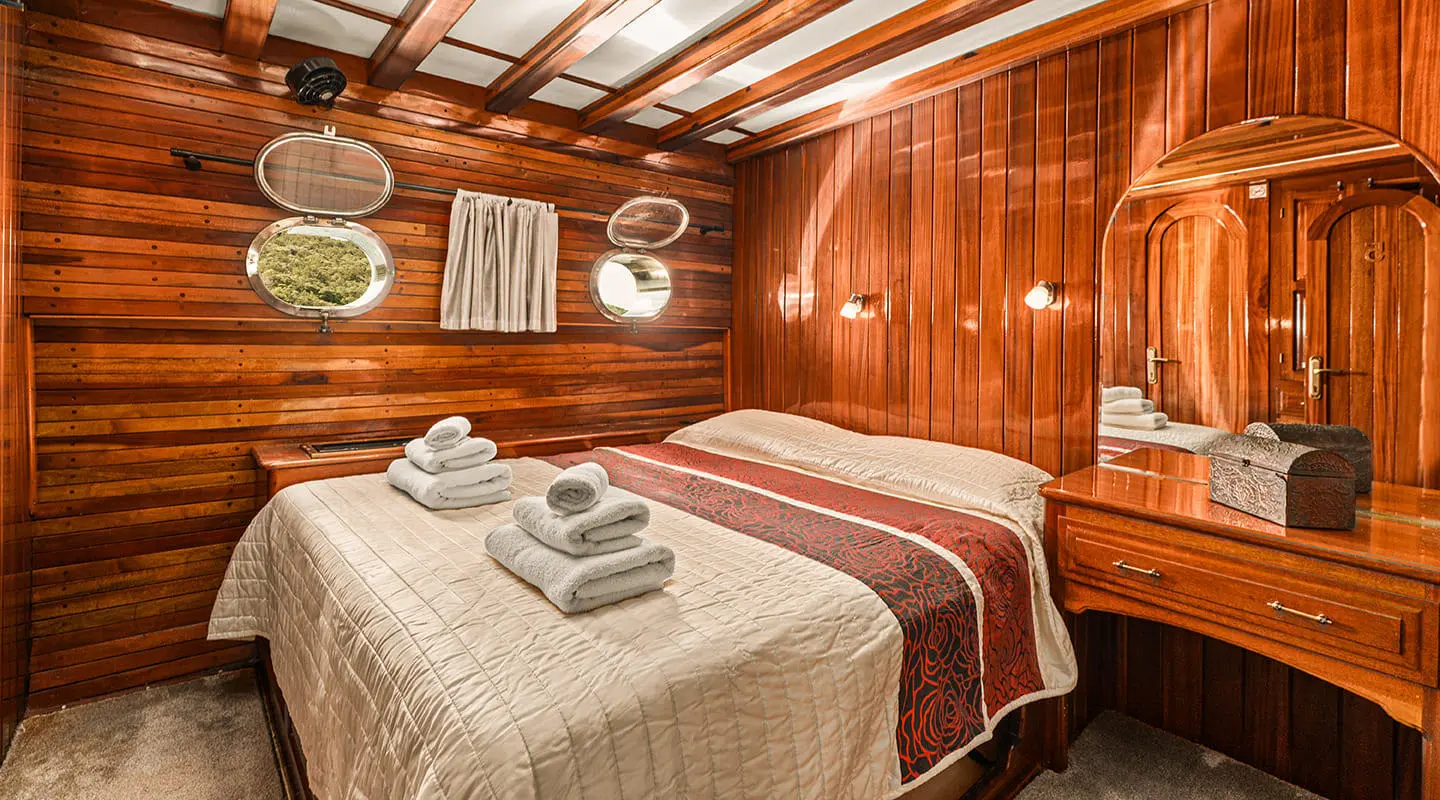 Two neatly made beds with beige and burgundy linens in a wood-paneled cabin