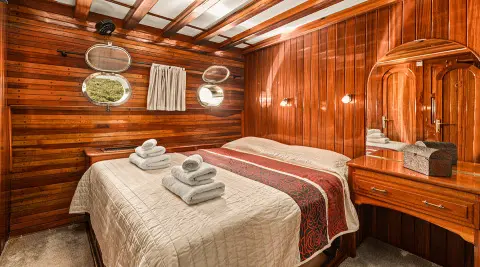 Two neatly made beds with beige and burgundy linens in a wood-paneled cabin