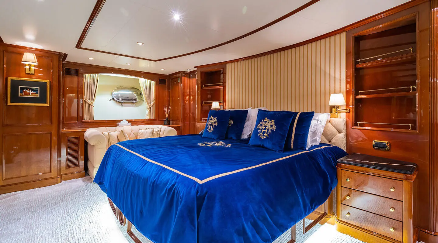 Amadea yacht bedroom with blue bedding, polished wood cabinets, and porthole light