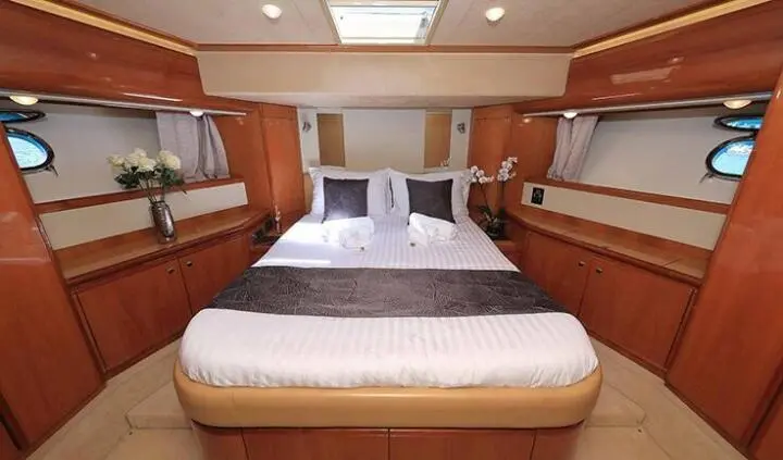 Quo Vadis I master cabin: neatly made bed with wood-paneled walls and porthole windows