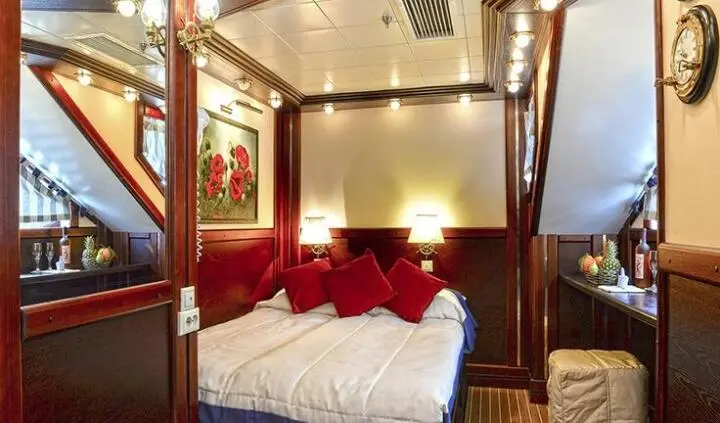 Luxurious double cabin aboard running on waves yacht with red bedding and wood paneling