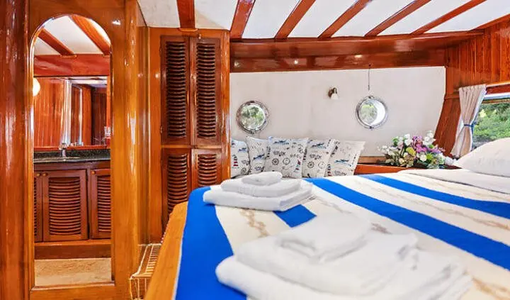 A yacht cabin with a large bed, blue linens, and towels on a bench