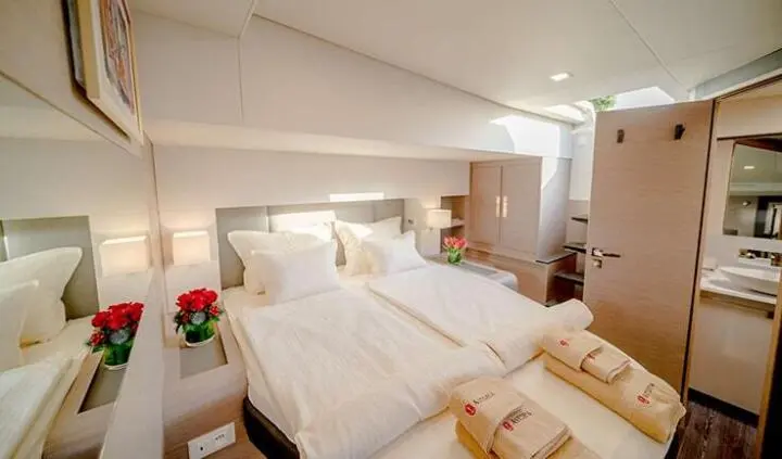 Astoria cabin with a large bed, white linens, and bedside lamps in yacht interior