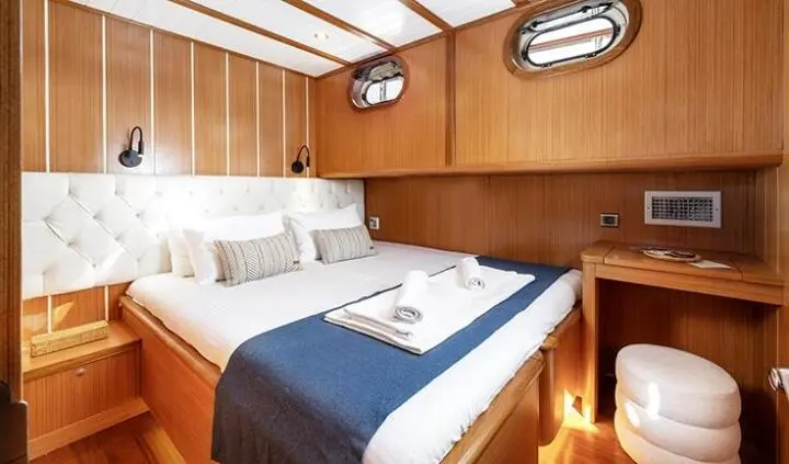 Master cabin with king bed, navy throw, wooden panels, reading lamps