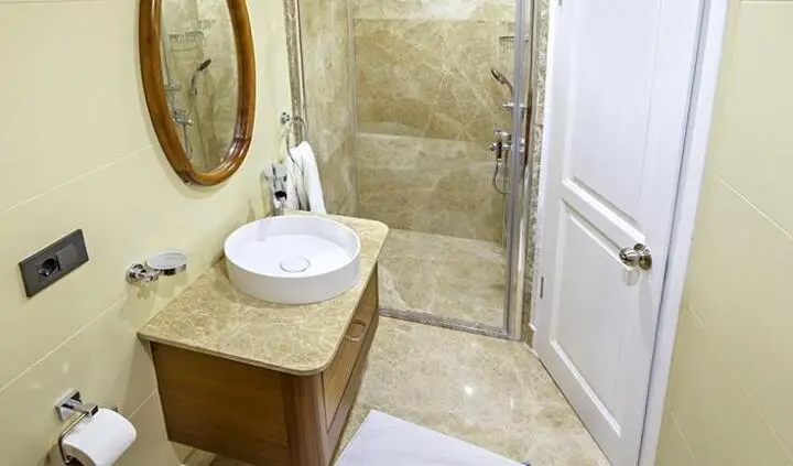 Bella Mare cabin interior with marble vanity, vessel sink, round mirror, and glass shower
